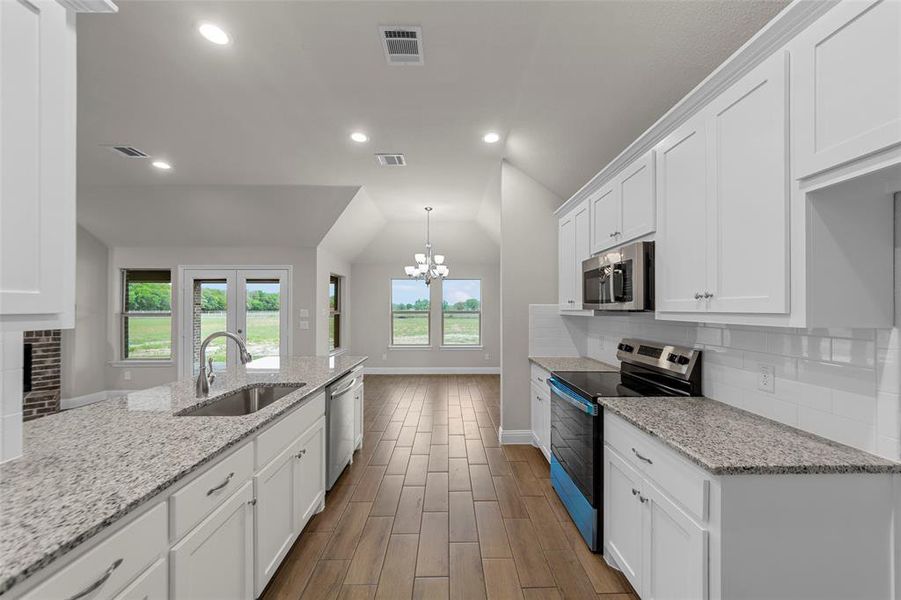 Kitchen featuring a deep stainless steel sink, granite-style countertops, wood-finish flooring, white cabinetry, and stainless steel appliances