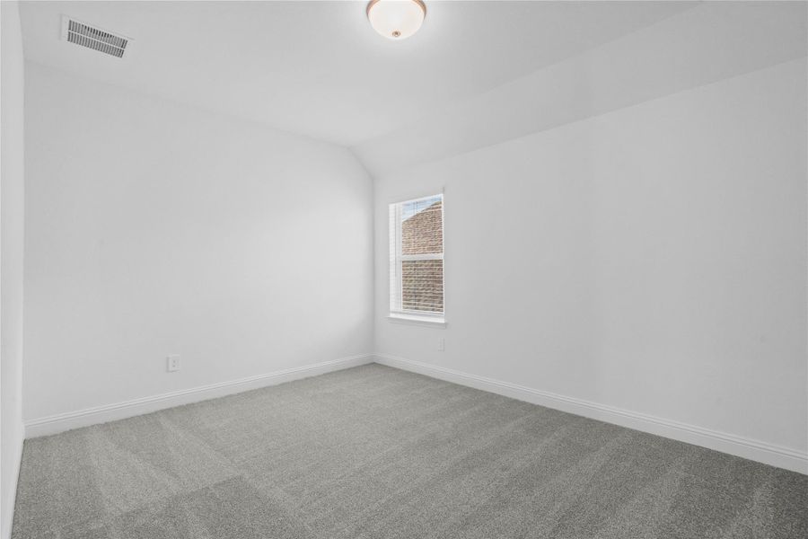This inviting secondary bedroom combines comfort and modern elegance, featuring plush carpeting, a neutral color palette, and abundant natural light streaming through a large window with blinds.