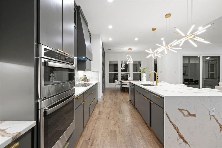 Kitchen with light wood-style flooring, stainless steel appliances, a sink, a large island, and pendant lighting