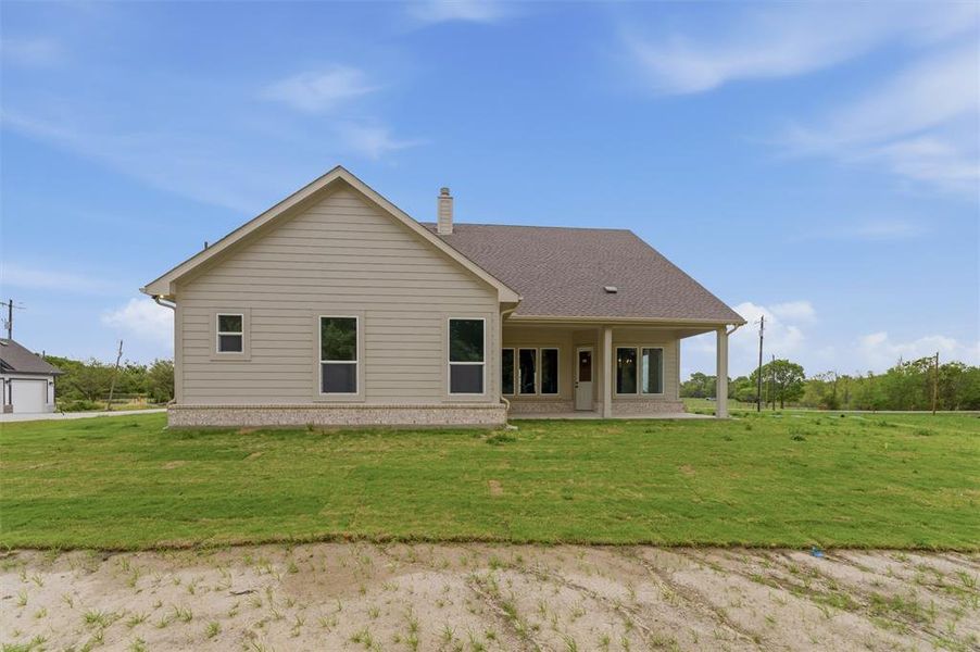 Back of property featuring a yard, a patio area, a chimney, and roof with shingles