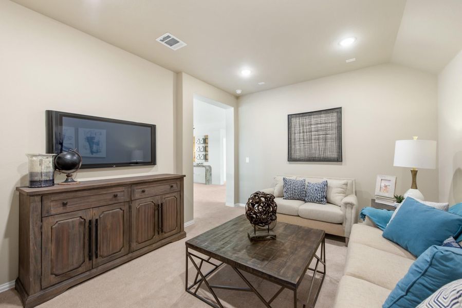 Living room with wall-mounted TV, wood media console, neutral sofas with blue accent pillows, and carpeted floors Living room with wall-mounted TV, wood media console, neutral sofas with blue accent pillows, and carpeted floors
