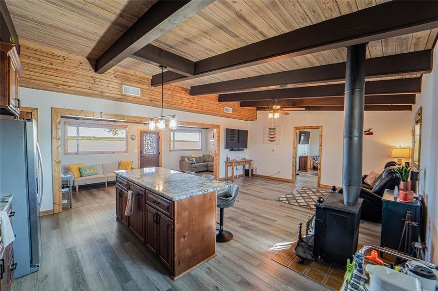 Kitchen with open floor plan, a center island, dark wood finished floors, light stone countertops, and a wood stove Kitchen with open floor plan, a center island, dark wood finished floors, light stone countertops, and a wood stove