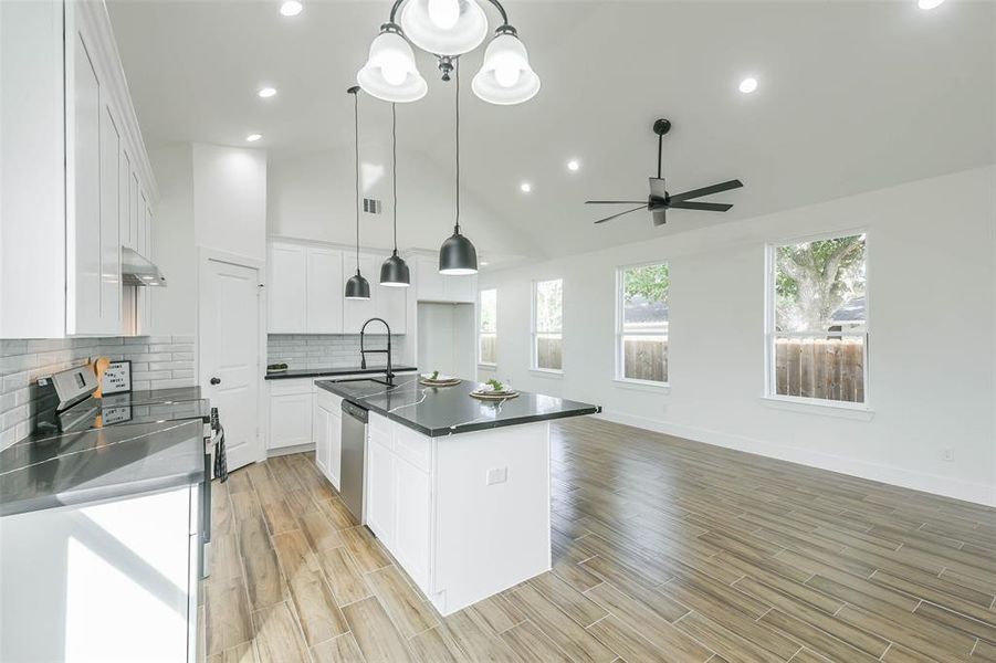 Modern, open-concept kitchen with sleek white cabinetry, stainless steel appliances, and a central island. Features wood flooring, pendant lighting, and ample natural light from large windows.