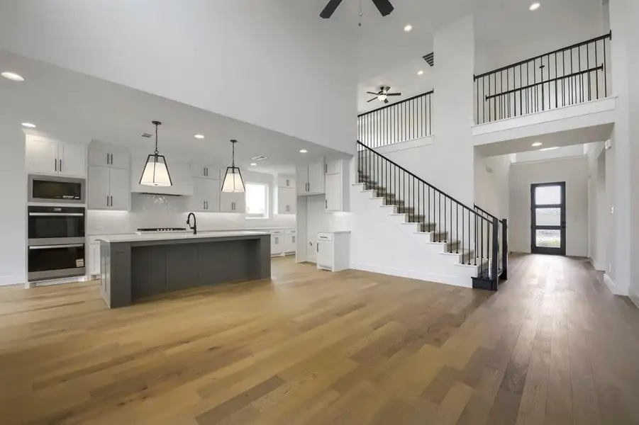 Open-concept living area with wood-finish flooring, a two-story ceiling, and a modern kitchen Open-concept living area with wood-finish flooring, a two-story ceiling, and a modern kitchen