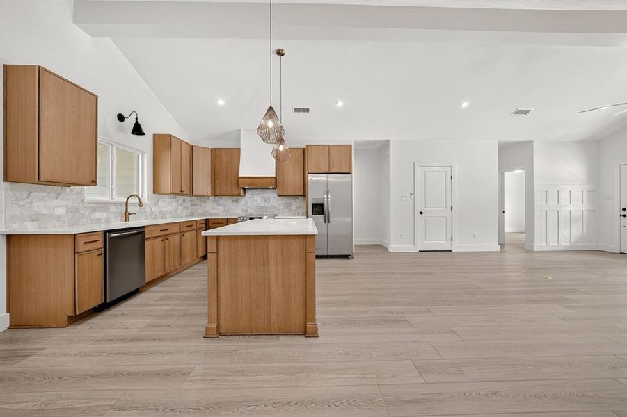 Spacious kitchen featuring light wood-finish cabinetry, white marble-look countertops, and a full tile backsplash