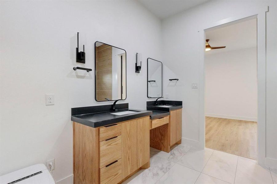 Double vanity featuring wood-finish cabinetry, dark countertops, and matte black fixtures Double vanity featuring wood-finish cabinetry, dark countertops, and matte black fixtures