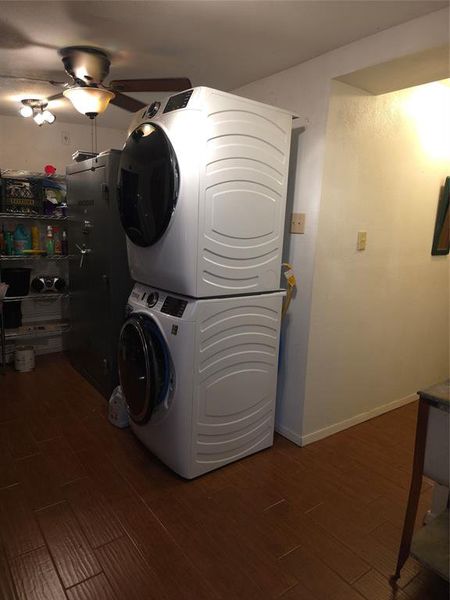 Washroom with dark wood-style flooring, stacked washer / dryer, and ceiling fan Washroom with dark wood-style flooring, stacked washer / dryer, and ceiling fan