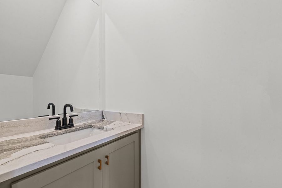 Vanity with an integrated rectangular sink, stone countertop, matte black faucet, and cabinet storage with brass hardware