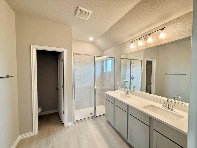 Bathroom with a stall shower, lofted ceiling, double vanity, a textured ceiling, and recessed lighting Bathroom with a stall shower, lofted ceiling, double vanity, a textured ceiling, and recessed lighting