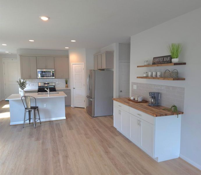Kitchen with butcher block countertops, tasteful backsplash, stainless steel appliances, open shelves, and light wood-type flooring