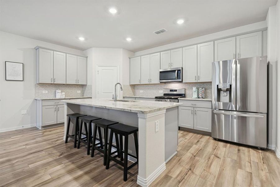 Kitchen with appliances with stainless steel finishes, a breakfast bar area, light stone counters, decorative backsplash, and recessed lighting