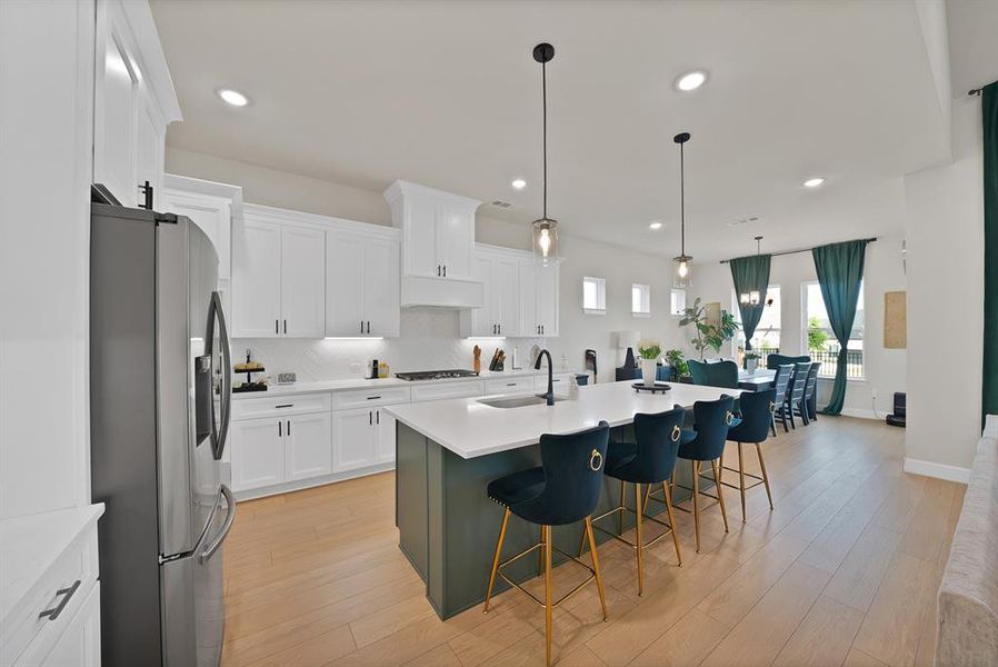 Open-concept kitchen featuring an oversized island with seating, white shaker cabinetry, stainless steel appliances, and wood-finish flooring Open-concept kitchen featuring an oversized island with seating, white shaker cabinetry, stainless steel appliances, and wood-finish flooring
