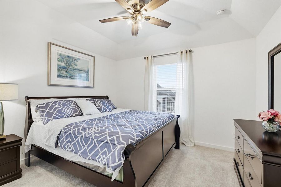This bedroom offers carpeted floors, a window for natural light, a vaulted ceiling, and a ceiling fan, providing a comfortable and airy space.