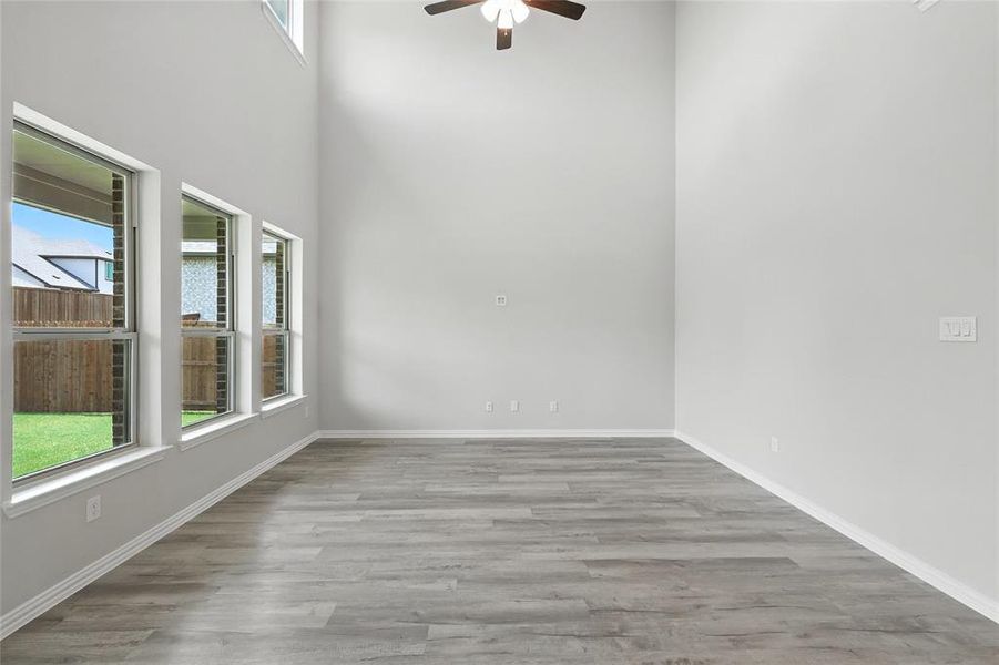 Unfurnished room with plenty of natural light, a ceiling fan, wood finished floors, and a towering ceiling Unfurnished room with plenty of natural light, a ceiling fan, wood finished floors, and a towering ceiling