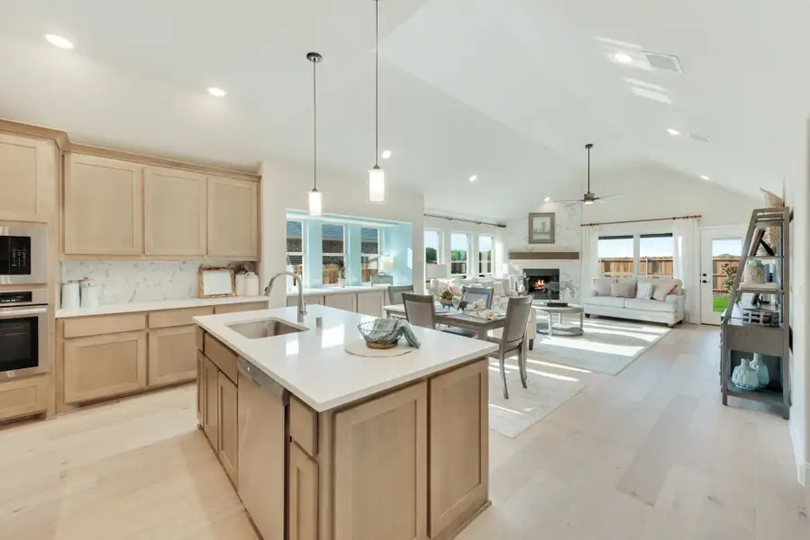 Open-concept kitchen with center island, light wood cabinets, and vaulted ceiling flowing into living and dining areas