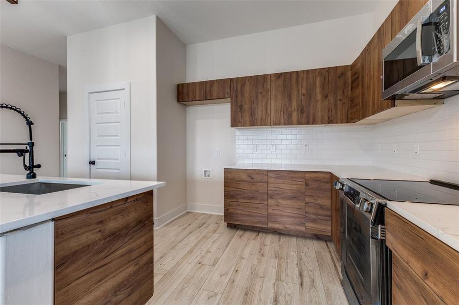 Kitchen featuring a sink, decorative backsplash, electric range oven, stainless steel microwave, and modern cabinets