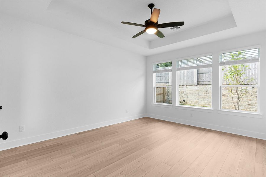 Spare room featuring a raised ceiling, light wood-type flooring, and ceiling fan