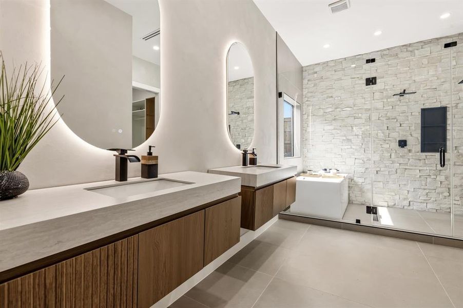 Contemporary bathroom featuring dual floating wood-finish vanities with integrated sinks, back-lit oval mirrors, a spacious walk-in shower with stone-stacked wall, and a freestanding soaking tub