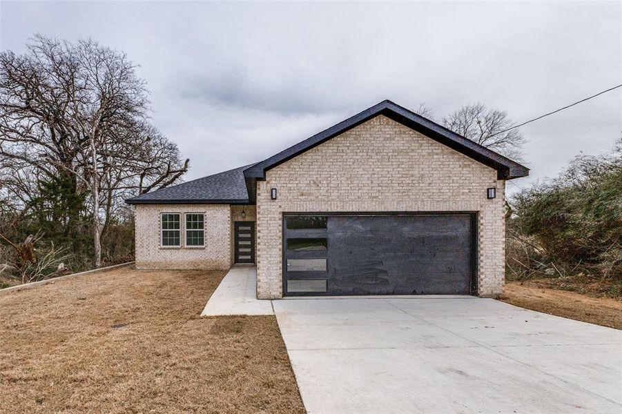 View of front of house featuring driveway, roof with shingles, a front yard, an attached garage, and brick siding