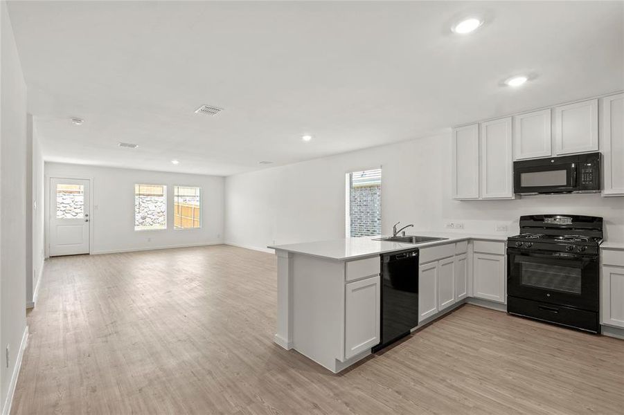 Open-concept kitchen and living area featuring wood-finish flooring, white cabinetry, a kitchen island with sink, and black appliances