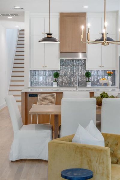 Kitchen with decorative backsplash, decorative light fixtures, and white cabinetry