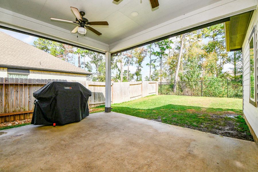This photo showcases a covered patio with two ceiling fans and a spacious backyard. It's ideal for outdoor entertaining and relaxation, with privacy provided by a wooden fence and a view of trees beyond. This photo showcases a covered patio with two ceiling fans and a spacious backyard. It's ideal for outdoor entertaining and relaxation, with privacy provided by a wooden fence and a view of trees beyond.