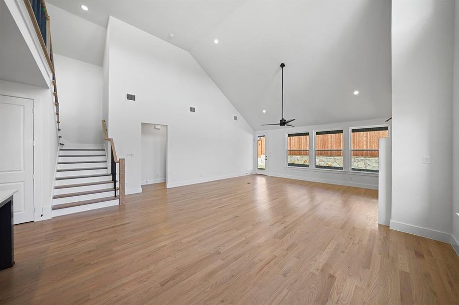 Unfurnished living room featuring high vaulted ceiling, recessed lighting, a ceiling fan, light wood-style floors, and stairs Unfurnished living room featuring high vaulted ceiling, recessed lighting, a ceiling fan, light wood-style floors, and stairs