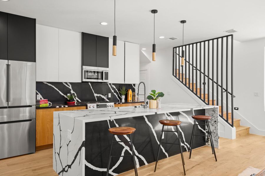 Modern kitchen with stainless steel appliances, modern cabinets, light wood-style flooring, an island with sink, and a kitchen breakfast bar Modern kitchen with stainless steel appliances, modern cabinets, light wood-style flooring, an island with sink, and a kitchen breakfast bar