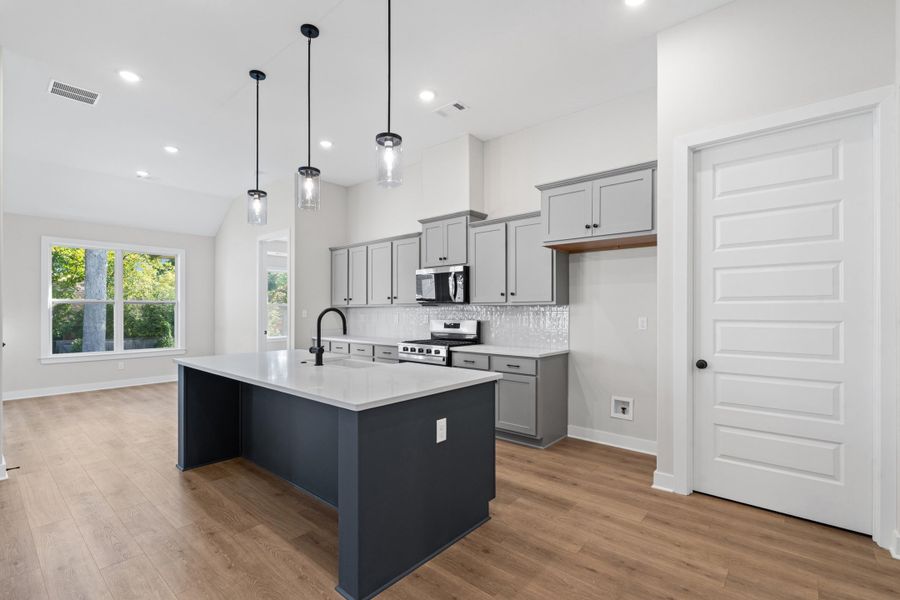 Kitchen featuring a center island, pendant lighting, wood-finish flooring, gray cabinetry, and a subway tile backsplash Kitchen featuring a center island, pendant lighting, wood-finish flooring, gray cabinetry, and a subway tile backsplash