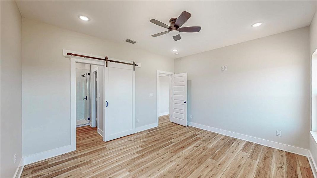 Unfurnished bedroom featuring a barn door, light wood-style floors, recessed lighting, and a ceiling fan Unfurnished bedroom featuring a barn door, light wood-style floors, recessed lighting, and a ceiling fan