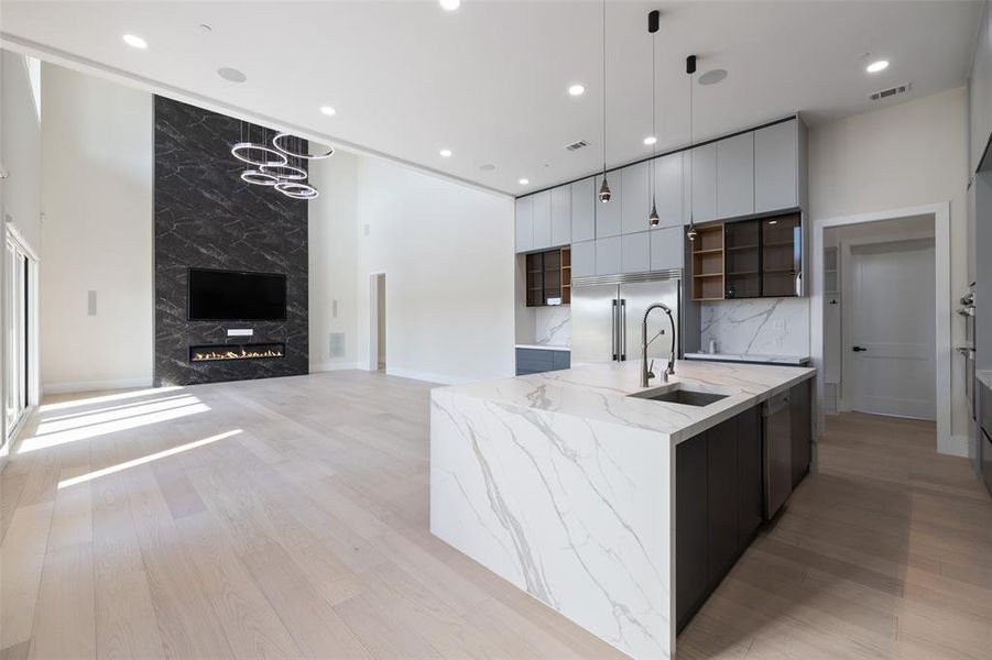 Kitchen featuring light hardwood / wood-style floors, dark brown cabinets, decorative light fixtures, sink, and a large island