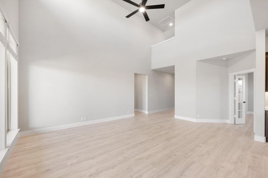 Empty living room with high vaulted ceiling, ceiling fan, and light wood floors Empty living room with high vaulted ceiling, ceiling fan, and light wood floors