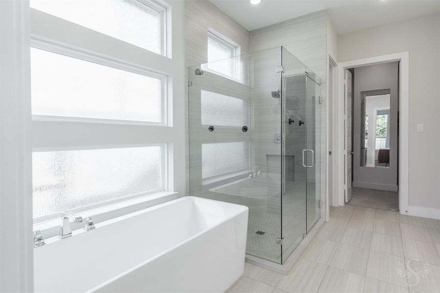 Freestanding soaking tub rests beneath a striking arrangement of frosted windows for privacy and natural light. An oversized walk-in shower with floor-to-ceiling tile and frameless glass creates a stunning companion feature. Freestanding soaking tub rests beneath a striking arrangement of frosted windows for privacy and natural light. An oversized walk-in shower with floor-to-ceiling tile and frameless glass creates a stunning companion feature.