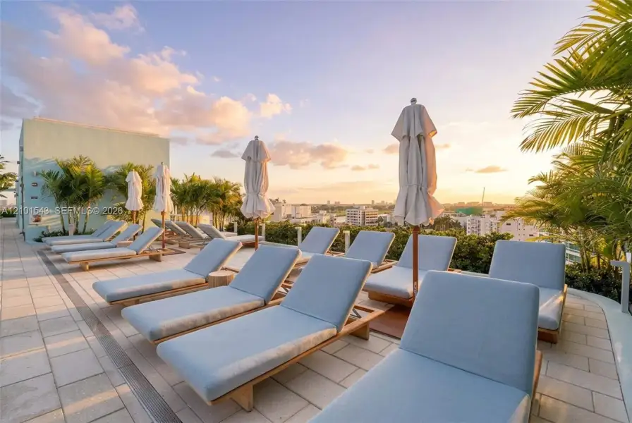 Rooftop terrace featuring light-toned stone tile flooring, perimeter landscaping with palm trees, and wide-reaching urban skyline scenery