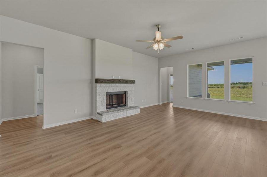 Spacious living area featuring wood-finish flooring, a white-painted brick fireplace with a wood mantle, and a ceiling fan Spacious living area featuring wood-finish flooring, a white-painted brick fireplace with a wood mantle, and a ceiling fan