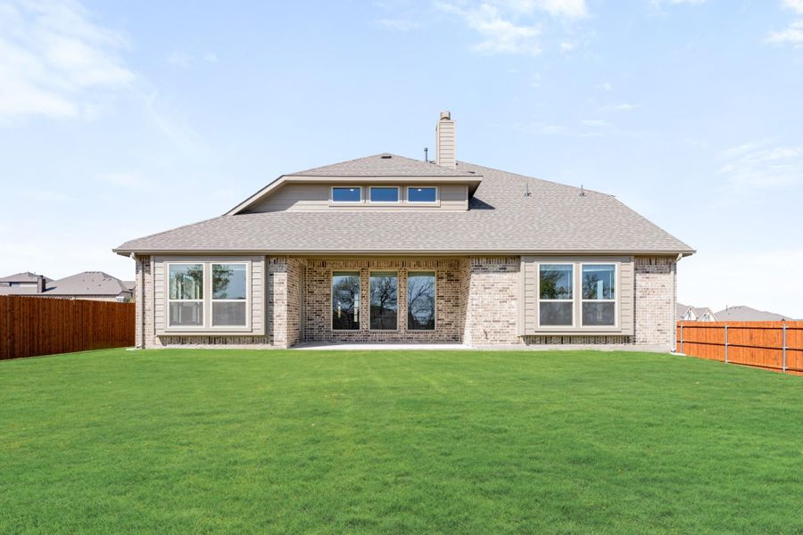 Rear view of brick home with large windows, chimney, patio doors, and fenced backyard with green lawn