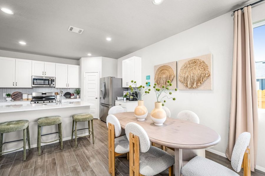 An image of the kitchen and dining area with wood flooring, a dining room with a tan dining table and white chair with wooden accents. An image of the kitchen and dining area with wood flooring, a dining room with a tan dining table and white chair with wooden accents.