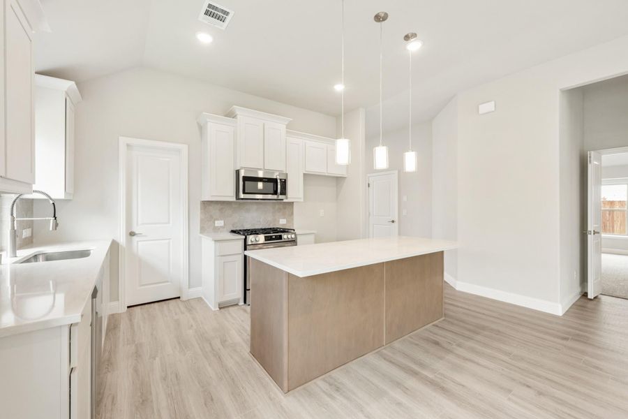 Kitchen with white cabinets, center island, stainless steel appliances, and light wood floors with pendant lighting Kitchen with white cabinets, center island, stainless steel appliances, and light wood floors with pendant lighting