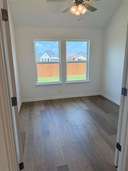 Room featuring wood-finish flooring, two large windows, a ceiling fan with integrated lighting, white baseboards, and neutral wall paint