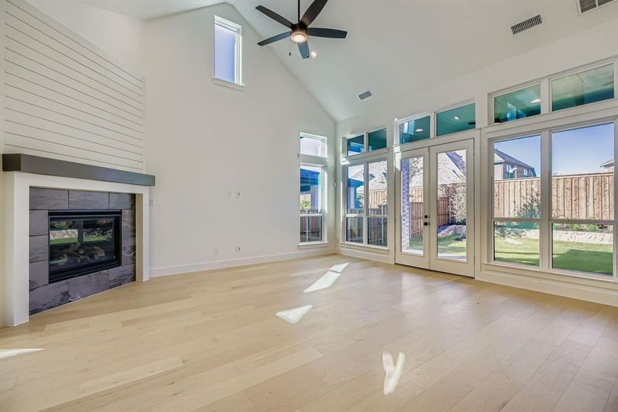 Unfurnished living room featuring high vaulted ceiling, french doors, light wood-style flooring, a tiled fireplace, and a ceiling fan