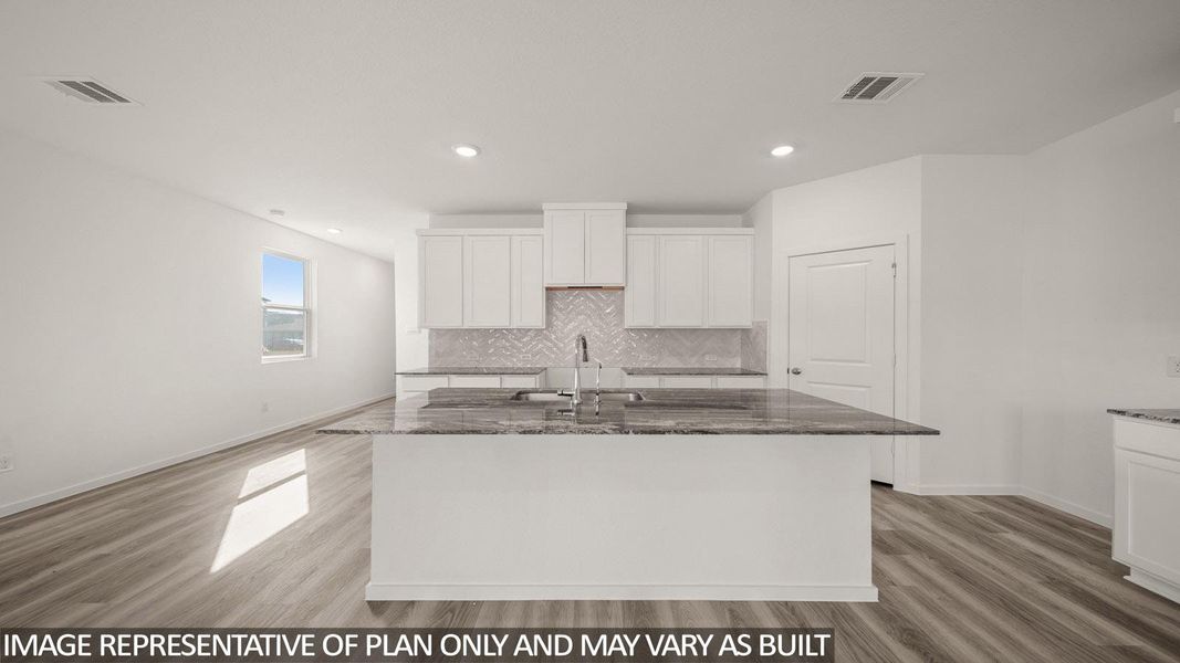 Kitchen island with integrated sink, stone countertop, white cabinetry, herringbone tile backsplash, and recessed lighting
