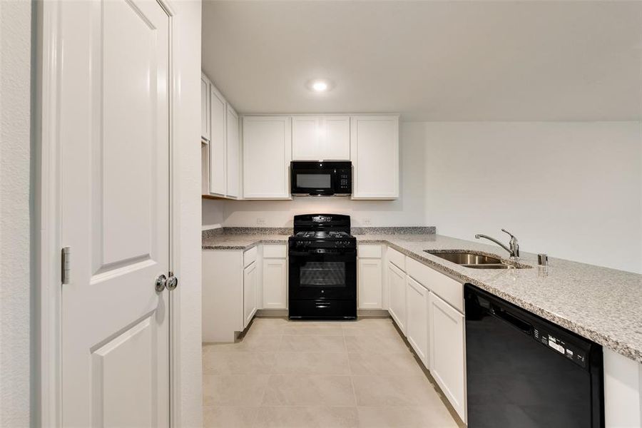 Kitchen featuring light tile patterned floors, white cabinets, black appliances, light stone countertops, and sink