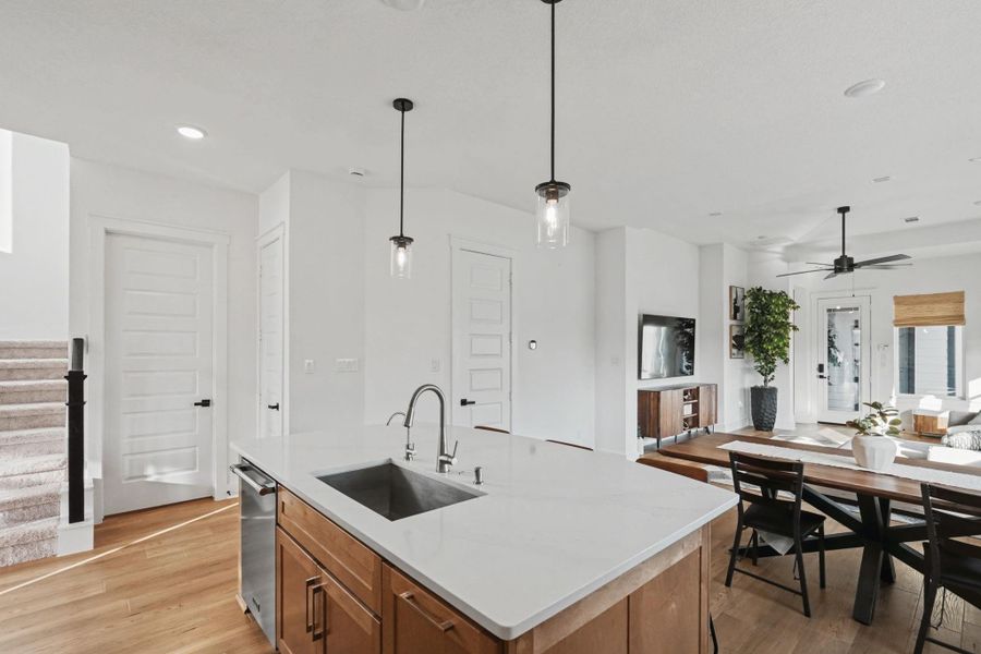 Impressive open-concept layout centered around a spacious quartz island with designer pendant lighting and warm wood flooring. The seamless flow between kitchen, dining, and living spaces creates a bright, sophisticated setting ideal for modern living.