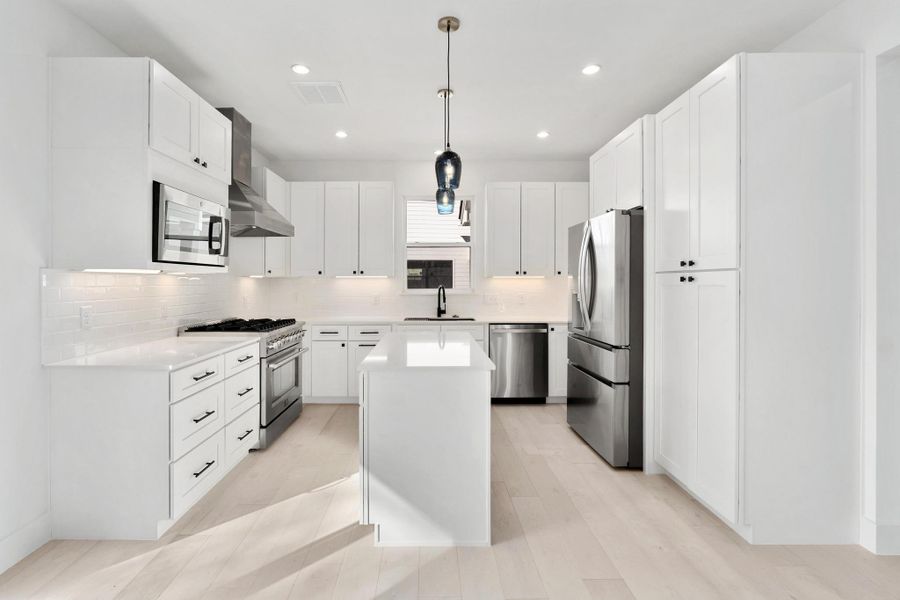 Kitchen with stainless steel appliances, white cabinetry, a center island, hanging light fixtures, and backsplash