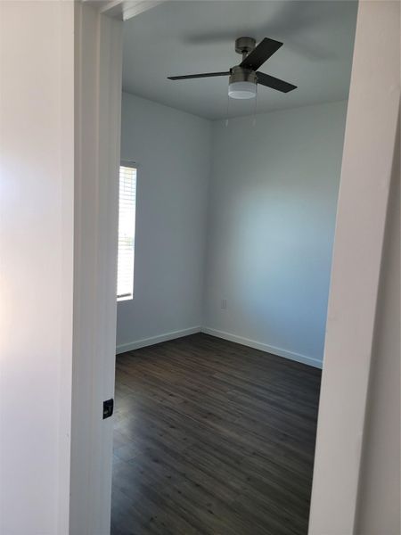 An inviting room features dark plank flooring, light walls, and a contemporary ceiling fan.