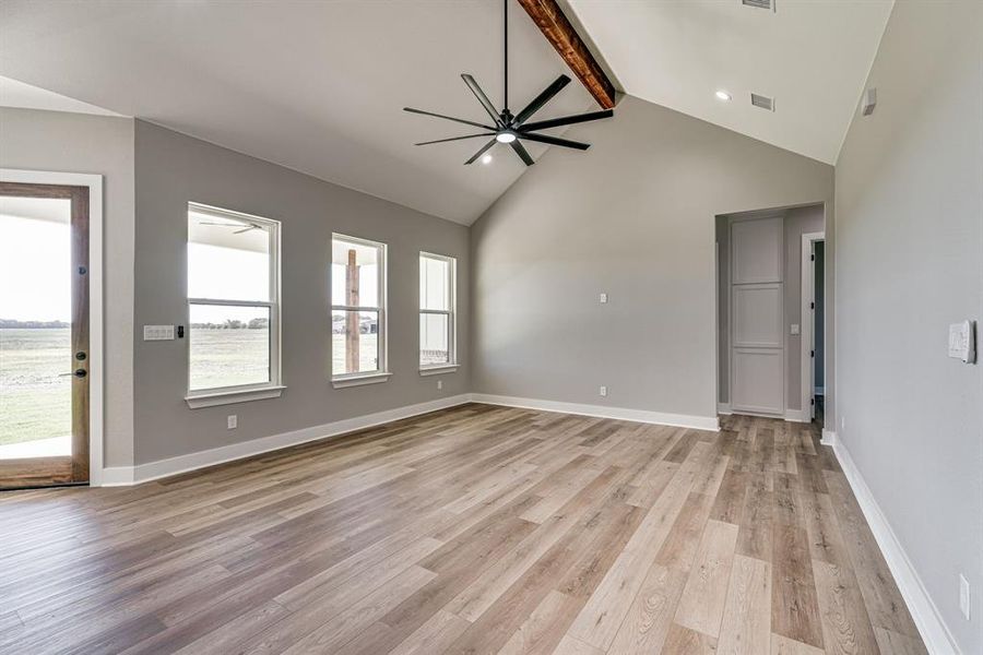 Unfurnished living room featuring light wood-type flooring, ceiling fan, beamed ceiling, and high vaulted ceiling