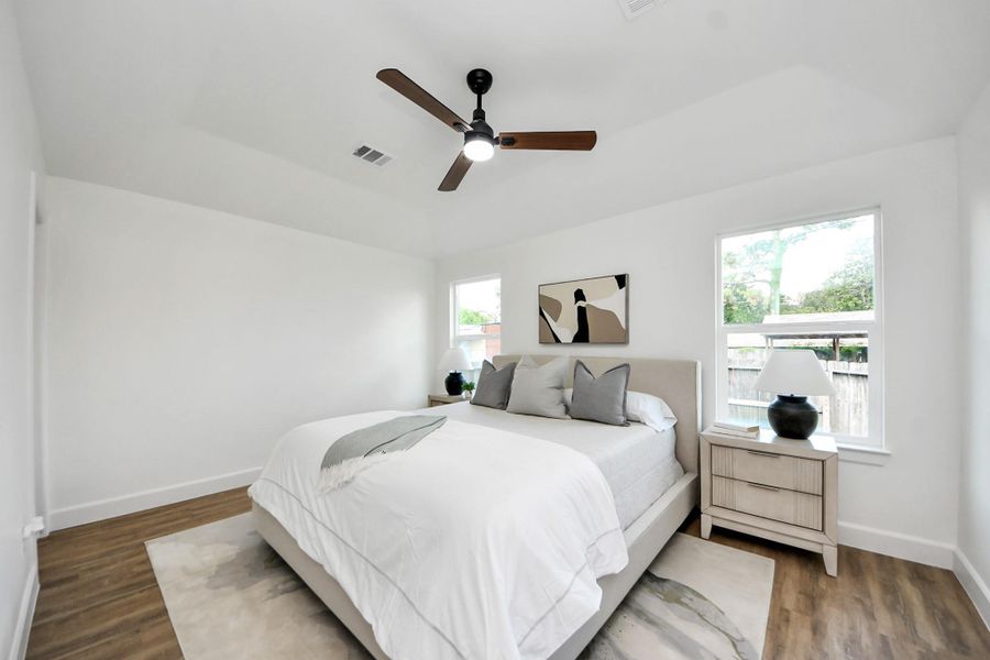 A serene, sunlit bedroom with vaulted ceilings that create an airy, restful retreat. Large windows invite in natural light, while neutral tones, a cozy bed, and simple, stylish touches complete the calm and inviting atmosphere.