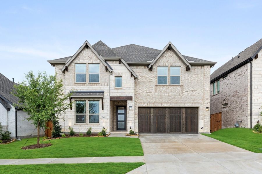 Two-story brick home with two-car garage, dark wood door, and manicured front lawn Two-story brick home with two-car garage, dark wood door, and manicured front lawn