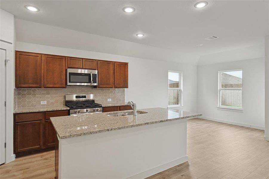 Kitchen with sink, appliances with stainless steel finishes, light wood-type flooring, and an island with sink