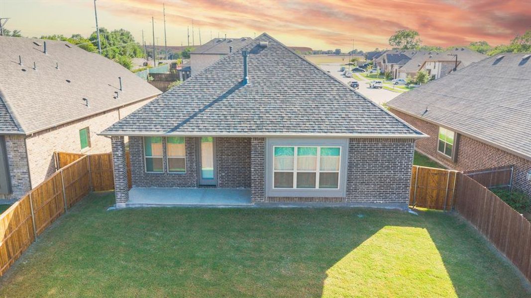 Back of property at dusk featuring roof with shingles, brick siding, and a fenced backyard